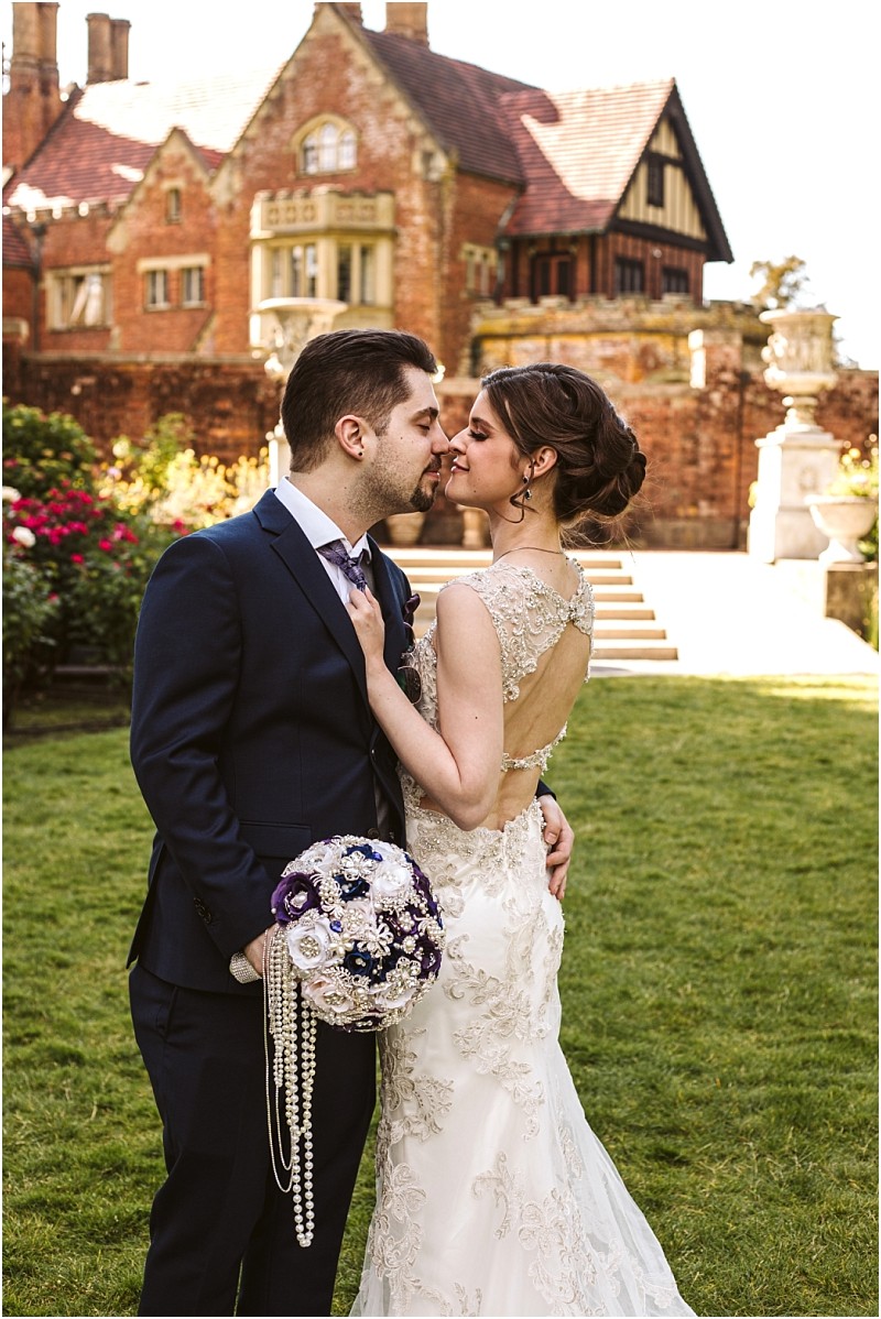 Premier snohomish & seattle wedding photographer | gsquared weddings photography a bride and groom stand close together gazing into each others eyes in a garden at a snohomish seattle wedding The bride holds a bouquet with pearls wearing an elegant lace gown with a historic brick building in the background | serving snohomish seattle                   & beyond