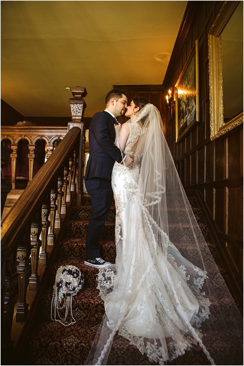 Premier snohomish & seattle wedding photographer | gsquared weddings photography a bride and groom share a kiss on a staircase at their elegant snohomish wedding The bride wears a long lace gown with a veil while the groom is in a suit with sneakers Wood paneling and paintings complete this seattle area love story | serving snohomish seattle                   & beyond
