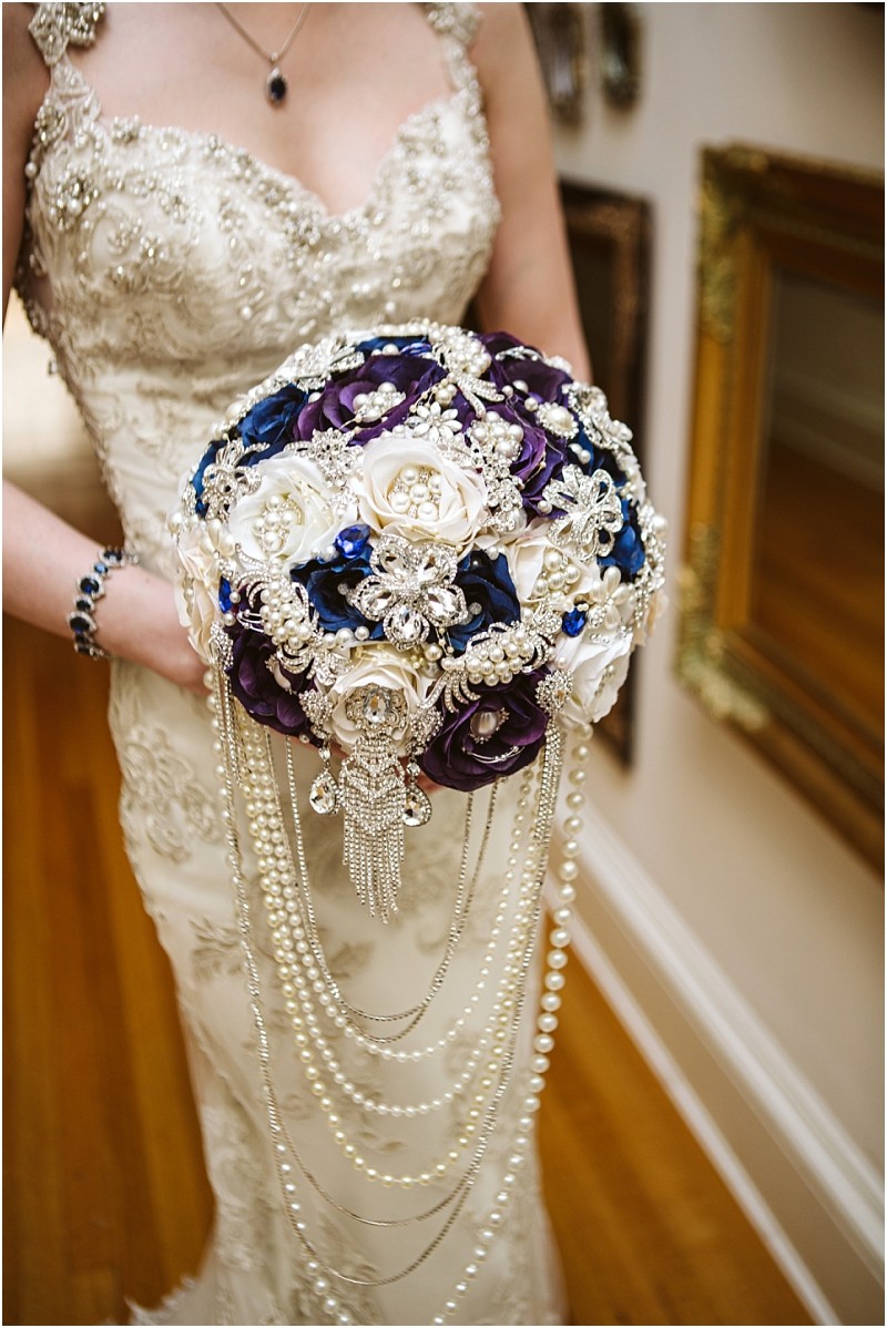 Premier snohomish & seattle wedding photographer | gsquared weddings photography a bride in an ornate lace dress holds a jeweled bouquet of white and purple fabric flowers perfect for a snohomish or seattle wedding Decorated with pearls brooches and cascading pearl strands she also wears a matching bracelet and necklace | serving snohomish seattle                   & beyond