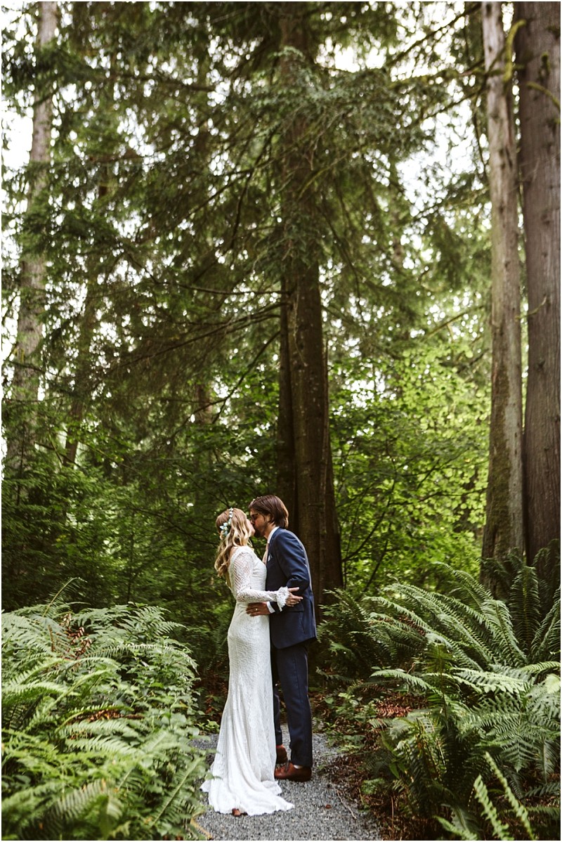 Premier snohomish & seattle wedding photographer | gsquared weddings photography a bride and groom embrace and kiss on a narrow path surrounded by lush green ferns and tall treesa magical snohomish forest setting perfect for a seattle wedding or engagement The bride wears a white long sleeve dress the groom a navy suit | serving snohomish seattle                   & beyond
