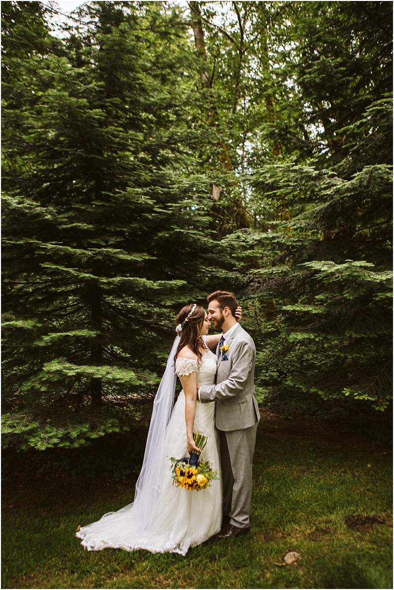 Premier snohomish & seattle wedding photographer | gsquared weddings photography a bride in a white dress and veil holding sunflowers stands close to her groom in a light gray suit They gaze at each other surrounded by tall green pine treesa magical snohomish wedding moment in a lush forest setting | serving snohomish seattle                   & beyond