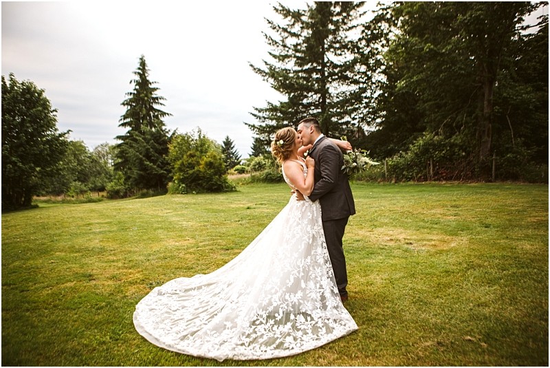 Premier snohomish & seattle wedding photographer | gsquared weddings photography a bride and groom embrace and kiss outdoors on a grassy lawn surrounded by trees at a charming snohomish seattle wedding The bride wears a flowing white lace gown and the groom is in a dark suit The scene is bright and natural | serving snohomish seattle                   & beyond
