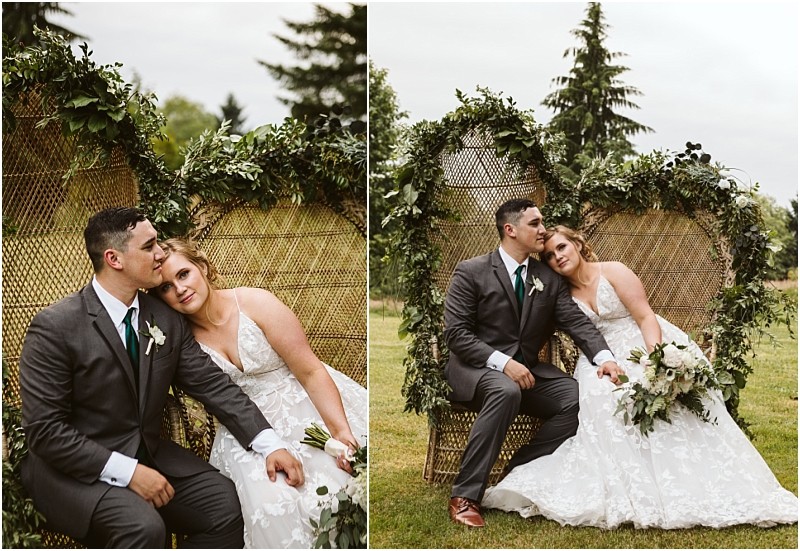 Premier snohomish & seattle wedding photographer | gsquared weddings photography a bride in a white lace dress and a groom in a gray suit sit closely on a greenery adorned wicker bench during their snohomish seattle wedding he kisses her forehead as she leans on his shoulder bouquet in hand | serving snohomish seattle                   & beyond