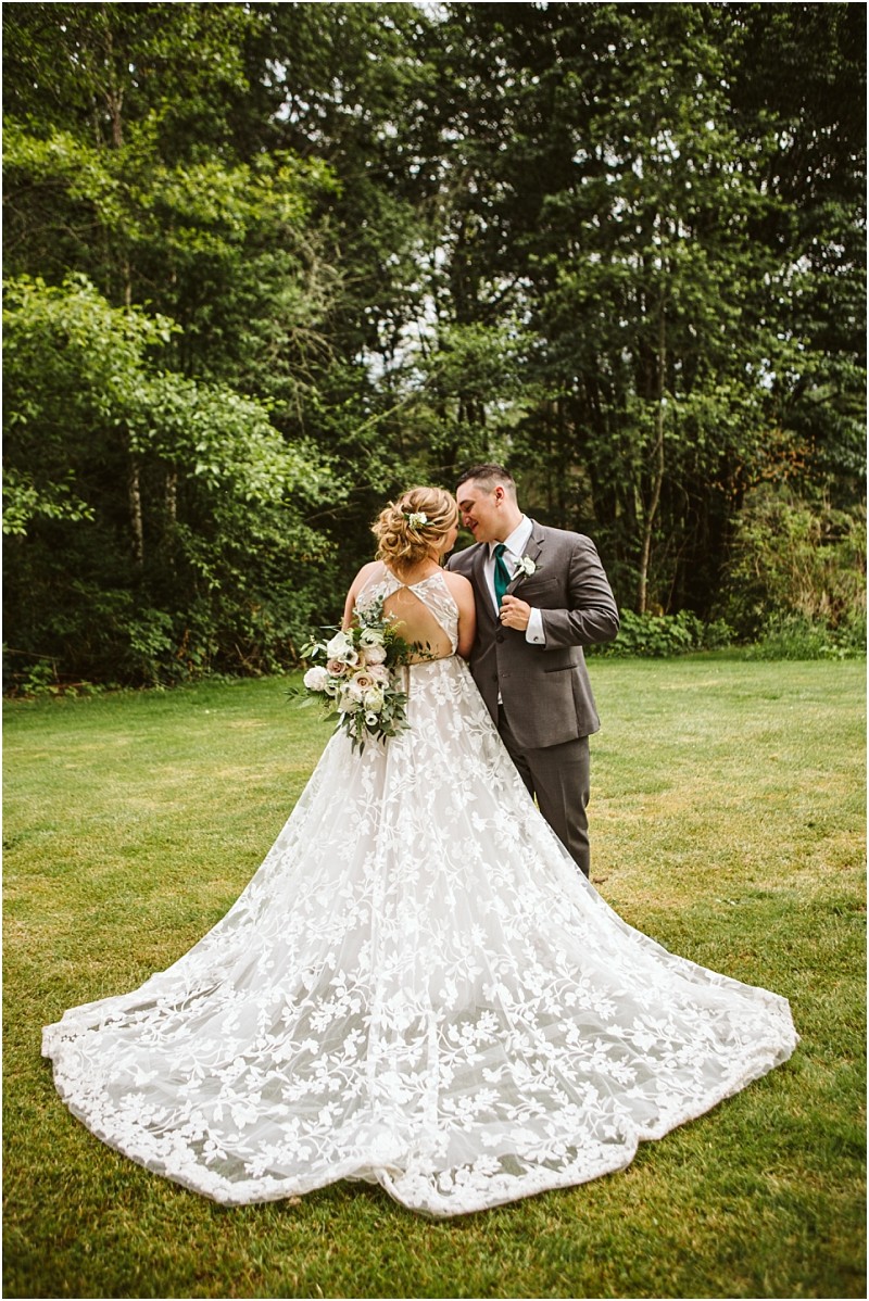 Premier snohomish & seattle wedding photographer | gsquared weddings photography a bride in a white lace gown holding a bouquet stands close to a groom in a gray suit and teal tie Surrounded by trees and green grass they share an affectionate moment during their snohomish seattle wedding | serving snohomish seattle                   & beyond