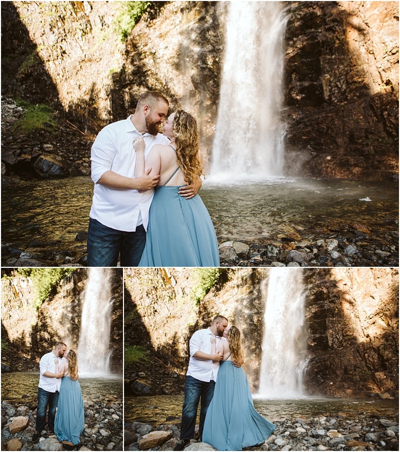 Premier snohomish & seattle wedding photographer | gsquared weddings photography a couple stands close together in front of a waterfall embracing and smiling during their snohomish engagement The woman wears a light blue dress the man a white shirt and jeans Sunlight illuminates the rocks and water behind them | serving snohomish seattle                   & beyond