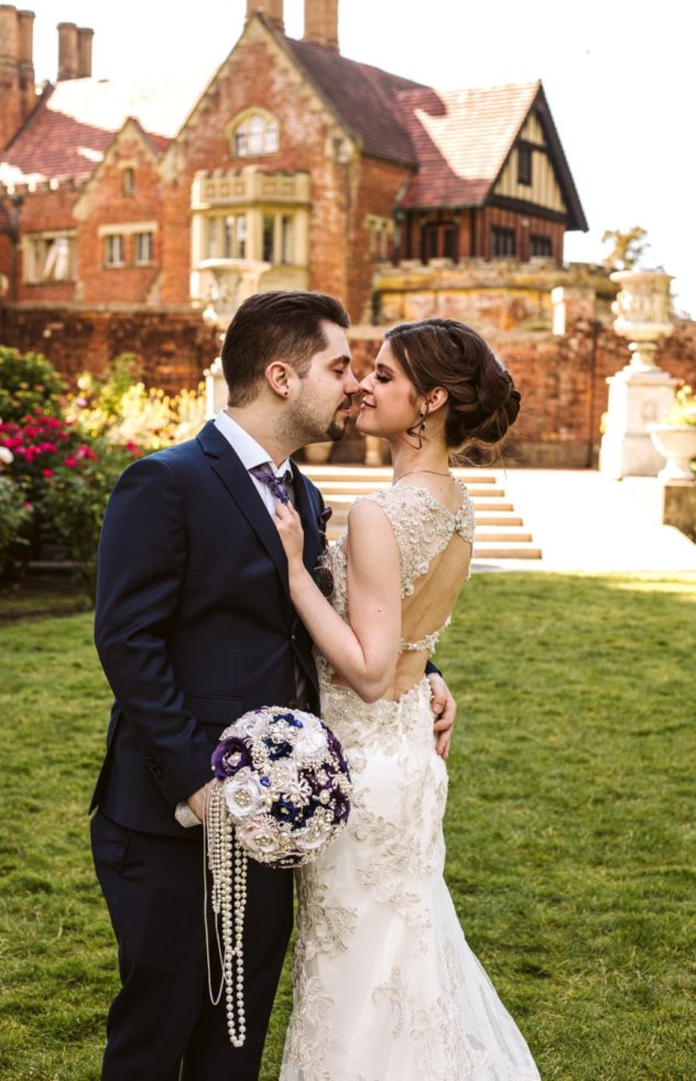 A bride and groom embrace and smile at each other outdoors in snohomish standing on grass in front of a large historic brick mansion The bride holds a bouquet decorated with pearls Snohomish wedding photography Washington wedding venue thornewood castle