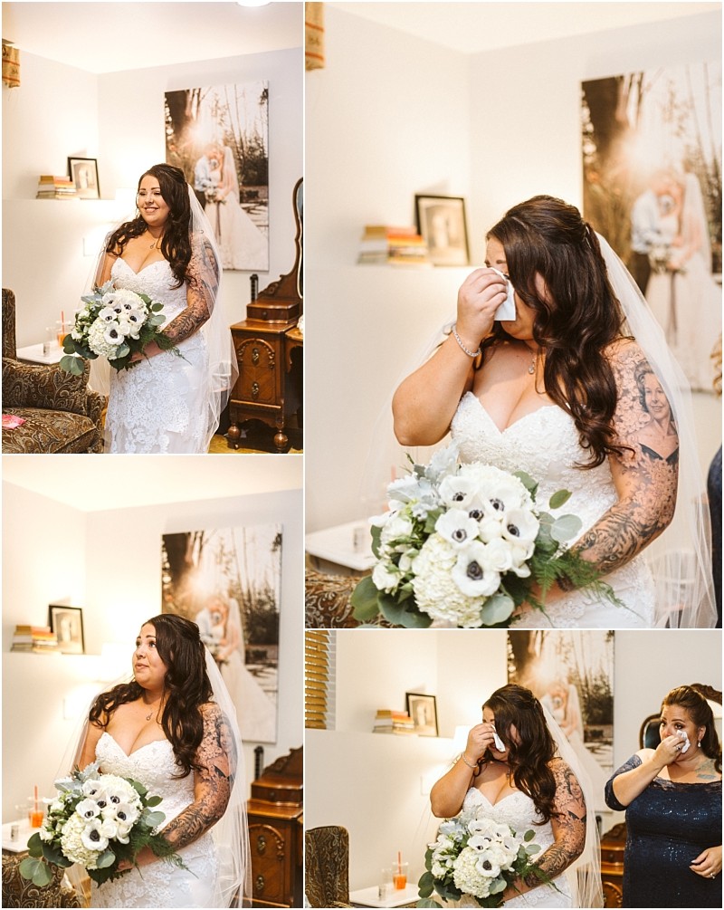 A bride in a white lace gown holds a bouquet of white flowers and wipes away tears emotional before her snohomish wedding An older woman stands behind her in support The room is warmly lit with personal decor in the background Snohomish wedding photography