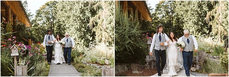 A bride in a white dress is walking outside on a garden path in snohomish smiling and holding a bouquet accompanied by two men in vests and ties one on each side of her They are surrounded by flowers and lush greenery Snohomish wedding photography
