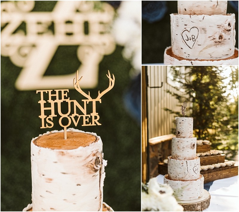 A rustic wedding cake in snohomish designed to look like birch tree trunks with the hunt is over antler topper and a heart engraved with j+b on the bark displayed outdoors amid lush greenery Snohomish wedding photography