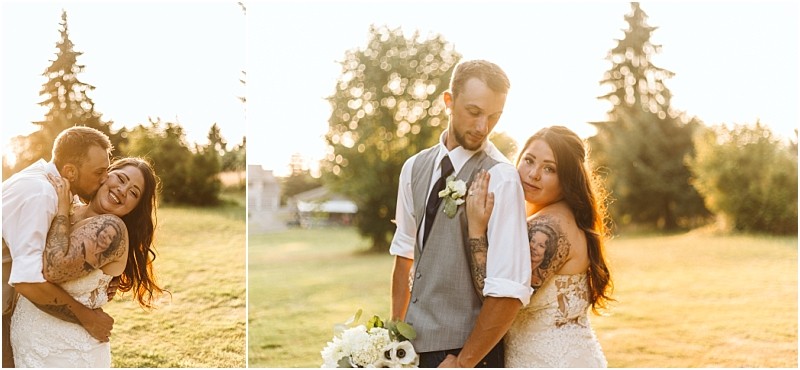 A bride and groom embrace outdoors at sunset in snohomish smiling and looking happy The bride has long hair and visible tattoos while the groom wears a vest and boutonniere They stand on green grass with trees in the background Snohomish wedding photography