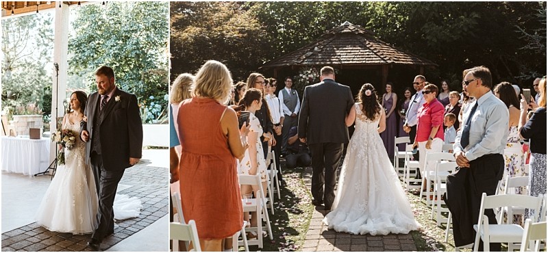 A bride in a white gown walks down the aisle with a man likely her father as guests seated on white chairs stand and watch during an outdoor wedding ceremony by a gazebo in snohomish Snohomish wedding photography
