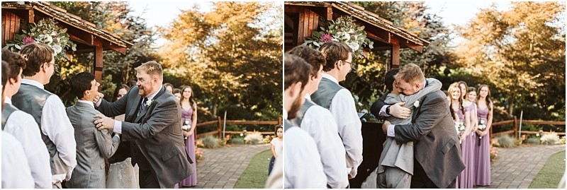 Two men in suits share an emotional moment at a snohomish outdoor wedding one wipes tears from the others face then they embrace tightly while bridesmaids in purple dresses watch in the background Snohomish wedding photography