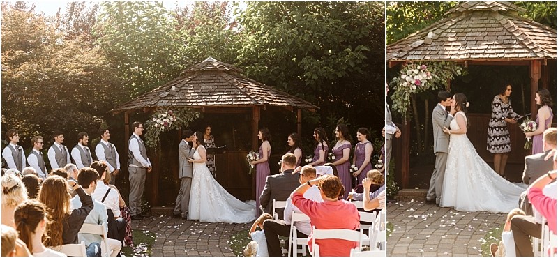 A bride and groom kiss at an outdoor snohomish wedding ceremony under a wooden gazebo surrounded by their wedding party and guests seated in white chairs on a sunny day Snohomish wedding photography