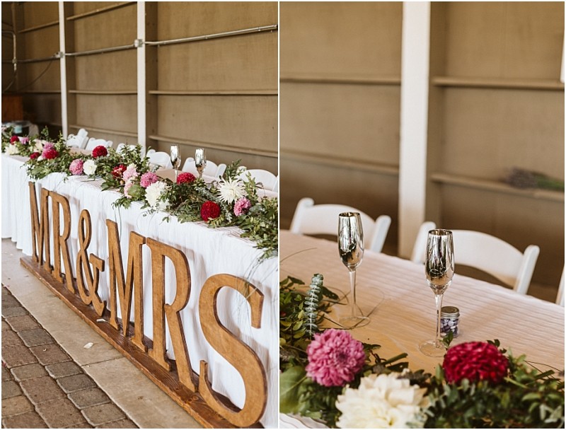 Wedding reception table in snohomish decorated with white cloth greenery and pink and white flowers Large wooden mr & mrs letters are displayed in front with champagne flutes and white chairs arranged behind the table Snohomish wedding photography