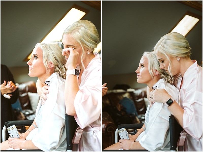 Two women with blonde hair wearing light pink robes sit closely together in a snohomish setting One woman hugs the other from behind and gently wipes away a tear creating an emotional and supportive atmosphere possibly during wedding preparation Snohomish wedding photography
