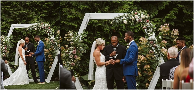 A bride and groom stand facing each other holding hands during an outdoor snohomish wedding ceremony They are under a geometric floral arch with a man officiating while guests are seated and watching Snohomish wedding photography