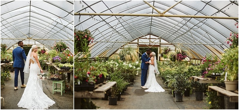 A bride and groom stand together in a snohomish greenhouse filled with green plants and flowers The bride wears a white dress with a long train while the groom in a blue suit embraces her beneath the arched glass roof Snohomish wedding photography