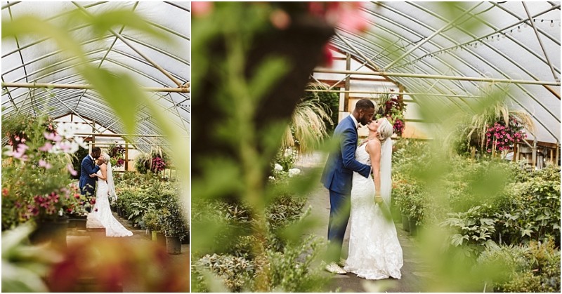 A bride and groom stand together in a lush snohomish greenhouse surrounded by vibrant plants and flowers The groom in a blue suit kisses the bride who wears a white lace gown as greenery frames the romantic scene Snohomish wedding photography