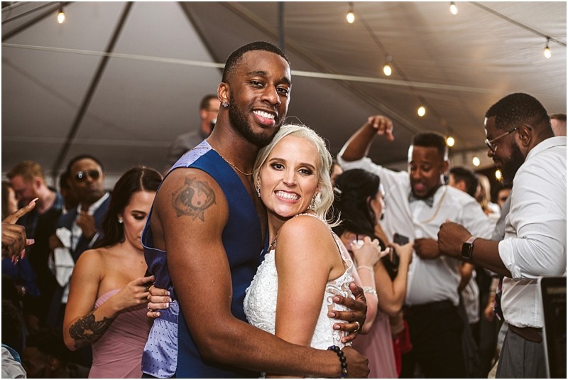 A smiling bride and groom embrace on the dance floor at their snohomish wedding reception surrounded by guests dancing and celebrating under string lights in a tent Snohomish wedding photography