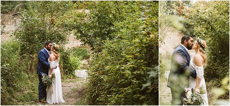 A bride and groom share a kiss on a narrow leafy path surrounded by snohomish greenery The bride wears a white dress and holds a bouquet while the groom stands beside her in a blue suit Snohomish wedding photography