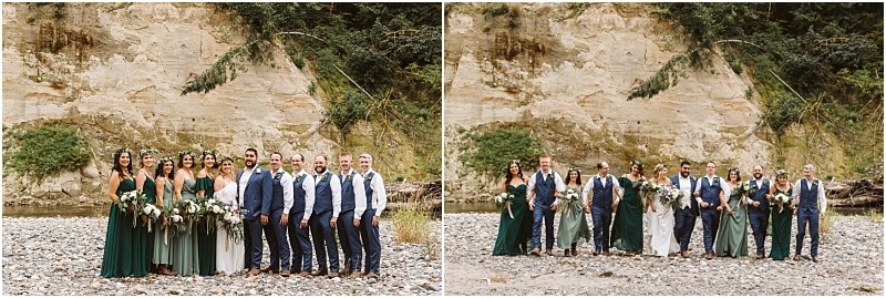 A wedding party poses outdoors on a rocky snohomish riverbank with forest and cliffs in the background The group includes people in green dresses and blue suits holding bouquets and smiling at the camera Snohomish wedding photography