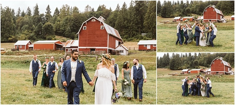 A bride and groom walk hand in hand with their wedding party through a green field in front of a large red barn surrounded by trees and rustic farm buildings in picturesque snohomish Snohomish wedding photography