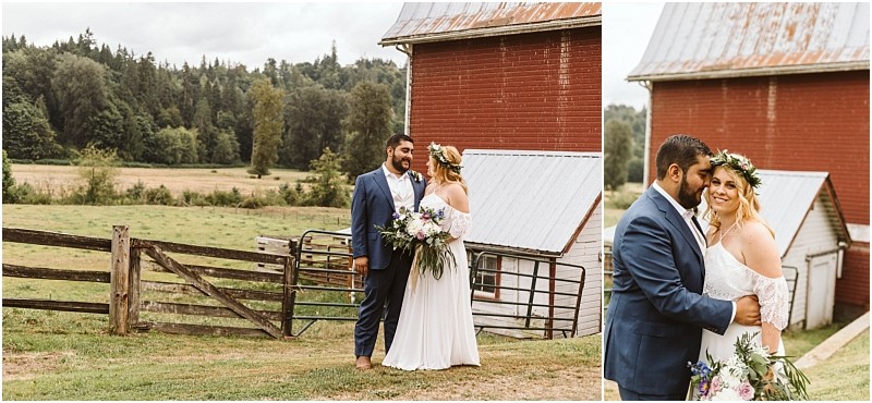 A bride and groom stand together outside a rustic red barn on a snohomish farm surrounded by green fields and trees The bride wears a flower crown and holds a bouquet both smile and gaze at each other lovingly Snohomish wedding photography