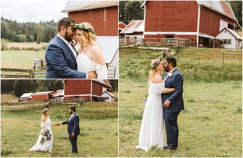 A bride and groom pose together outdoors near a red barn in snohomish embracing and holding hands in a grassy field surrounded by rustic farm buildings Snohomish wedding photography