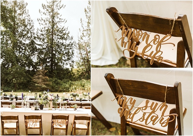 Outdoor wedding reception in snohomish with decorated wooden chairs signs on chairs read moon of my life and my sun and stars Long tables set with flowers and greenery framed by tall trees in the background Snohomish wedding photography