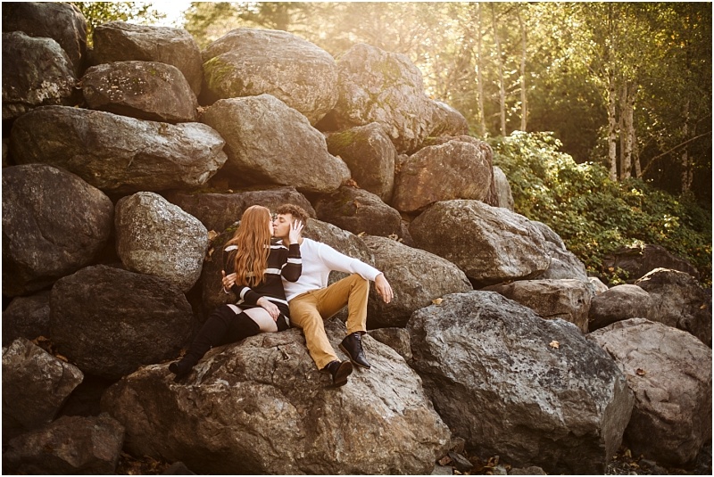 Premier snohomish & seattle wedding photographer | gsquared weddings photography a couple sits on large rocks outdoors in snohomish surrounded by greenery and sunlight Sharing a kiss the womans long red hair shines while the man dressed in tan pants and a white shirt creates a romantic seattle engagement moment | serving snohomish seattle & beyond Premier snohomish & seattle wedding photographer | gsquared weddings photography a couple sits on large rocks outdoors in snohomish surrounded by greenery and sunlight Sharing a kiss the womans long red hair shines while the man dressed in tan pants and a white shirt creates a romantic seattle engagement moment | serving snohomish seattle & beyond