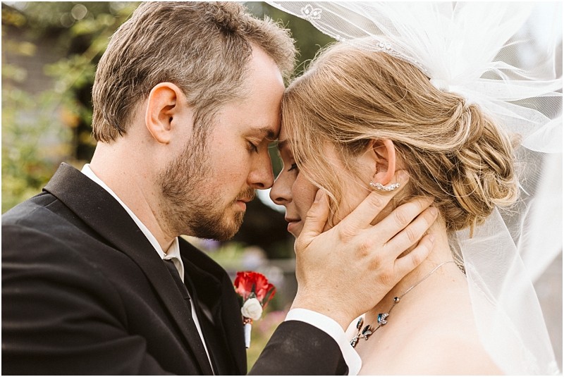 Premier snohomish & seattle wedding photographer | gsquared weddings photography a groom gently holds his brides face as they touch foreheads eyes closed in a tender moment Captured outdoors during their snohomish seattle wedding she wears a veil and necklace he dons a black suit with a red boutonniere | serving snohomish seattle                   & beyond