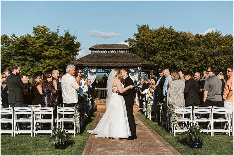 Premier snohomish & seattle wedding photographer | gsquared weddings photography a bride and groom kiss at the end of an outdoor aisle surrounded by cheering guests The wedding ceremony in snohomish takes place before a gazebo beneath a clear blue skycapturing the charm of a seattle wedding | serving snohomish seattle                   & beyond
