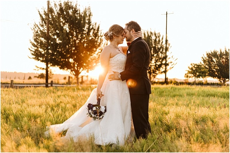 Premier snohomish & seattle wedding photographer | gsquared weddings photography bride and groom embrace in a grassy field at sunset during their snohomish wedding The bride holds a bouquet and wears a white strapless gown while the groom is in a dark suit Trees and golden sunlight create a warm romantic atmosphere | serving snohomish seattle                   & beyond