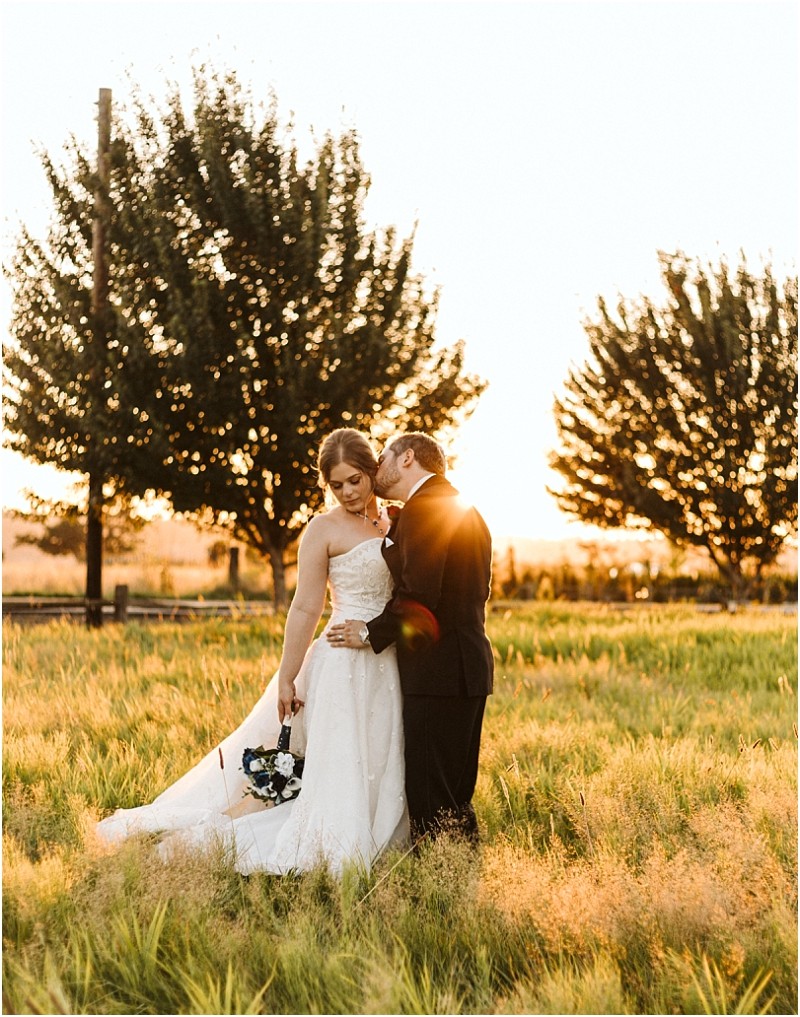 Premier snohomish & seattle wedding photographer | gsquared weddings photography a bride in a white gown holds a bouquet while the groom in a black suit kisses her cheek in a sunlit snohomish field with trees and golden light making their seattle wedding engagement unforgettable | serving snohomish seattle                   & beyond