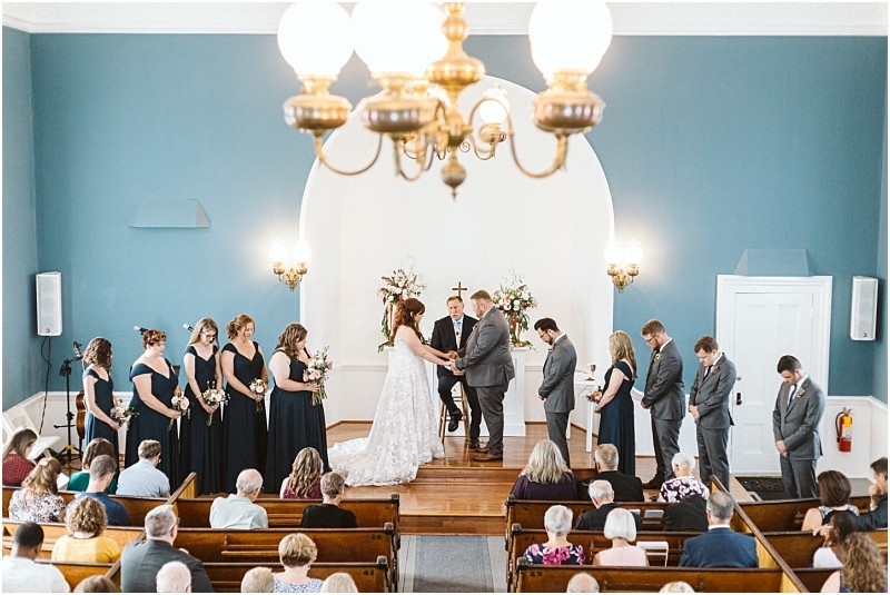 Premier snohomish & seattle wedding photographer | gsquared weddings photography a bride and groom stand at the altar in a church near snohomish surrounded by bridesmaids in navy dresses and groomsmen in gray suits while guests watch the wedding ceremony from wooden pews | serving snohomish seattle                   & beyond