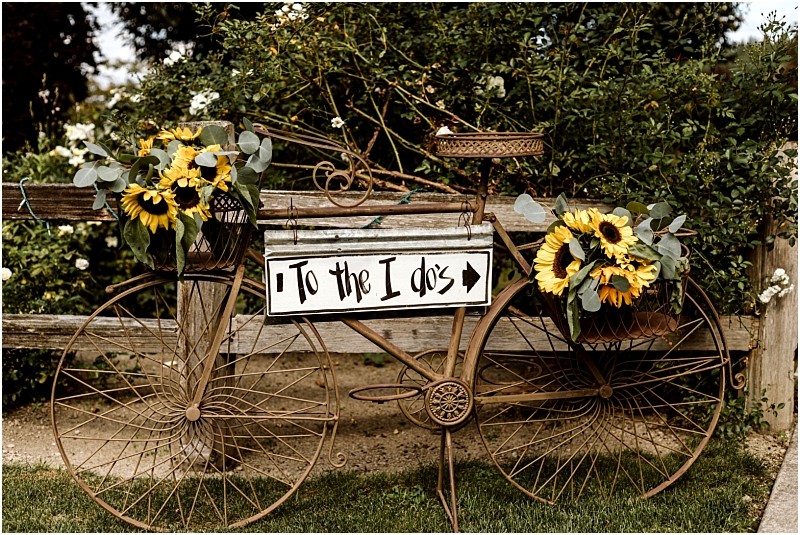Premier snohomish & seattle wedding photographer | gsquared weddings photography a decorative vintage bicycle with baskets of sunflowers and greenery leans against a wooden fence perfect for a snohomish or seattle wedding A white sign on the bike reads to the i dos with an arrow pointing right | serving snohomish seattle                   & beyond