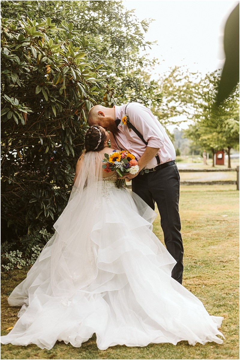 Premier snohomish & seattle wedding photographer | gsquared weddings photography a bride in a flowing white gown holding a bouquet stands under a tree as her groom gently kisses her forehead outdoorsa romantic snohomish seattle wedding engagement moment captured beautifully | serving snohomish seattle                   & beyond