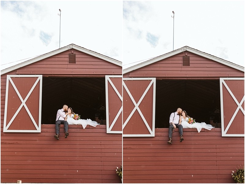 Premier snohomish & seattle wedding photographer | gsquared weddings photography a bride and groom sit in the open window of a red barn at their snohomish wedding sharing a kiss and holding a bouquet The brides white dress cascades over the edge with a partly cloudy sky above them | serving snohomish seattle                   & beyond