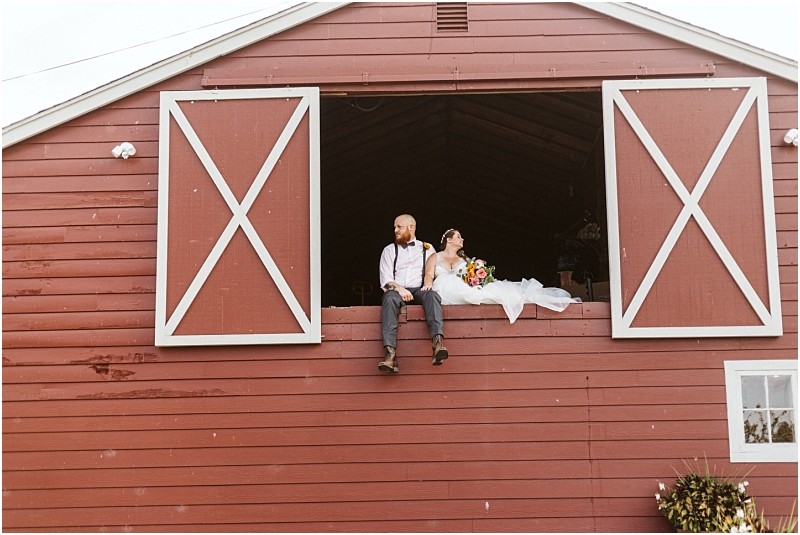 Premier snohomish & seattle wedding photographer | gsquared weddings photography a bride and groom sit in the open loft of a red barn with white trim capturing a relaxed and happy moment Perfect for a snohomish seattle wedding or engagement the groom wears suspenders while the bride holds a colorful bouquet | serving snohomish seattle                   & beyond