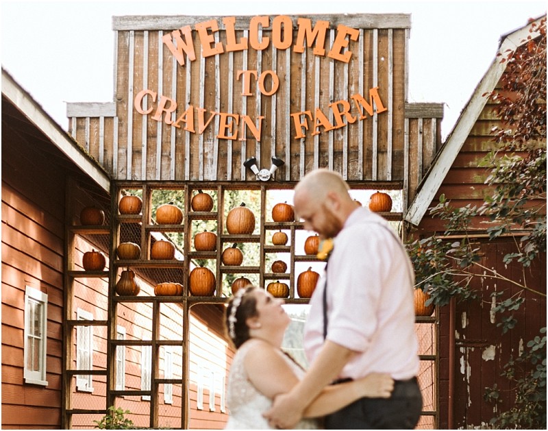 Premier snohomish & seattle wedding photographer | gsquared weddings photography a couple embraces and smiles at the rustic craven farm entrance in snohomish perfect for a seattle wedding engagement with pumpkins displayed on shelves behind them | serving snohomish seattle                   & beyond