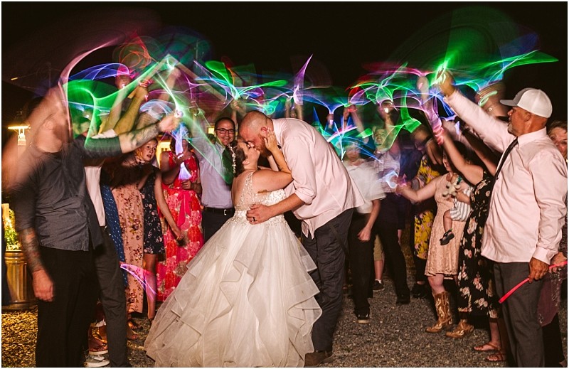 Premier snohomish & seattle wedding photographer | gsquared weddings photography a bride and groom kiss as they are surrounded by cheering guests waving colorful glow sticks in the air during a magical snohomish wedding celebration The bride wears a white gown and the groom is in a shirt and vest | serving snohomish seattle                   & beyond