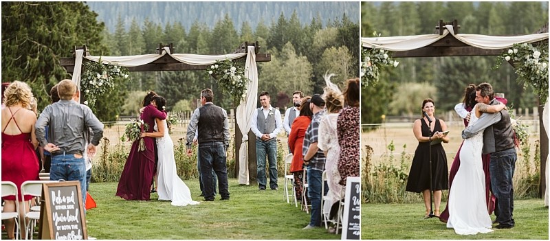 Premier snohomish & seattle wedding photographer | gsquared weddings photography outdoor snohomish wedding ceremony with a bride hugging a man under a flower adorned arch Guests watch from seated rows some standing Mountains and trees frame this beautiful seattle engagement moment | serving snohomish seattle                   & beyond
