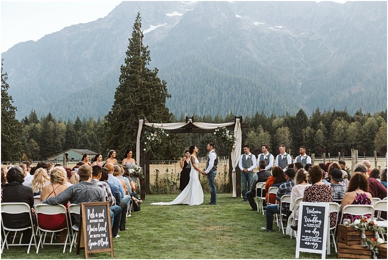 Premier snohomish & seattle wedding photographer | gsquared weddings photography a bride and groom stand under an arch during a romantic snohomish outdoor wedding ceremony surrounded by their wedding party and guests with mountains and trees creating a stunning seattle area backdrop | serving snohomish seattle                   & beyond