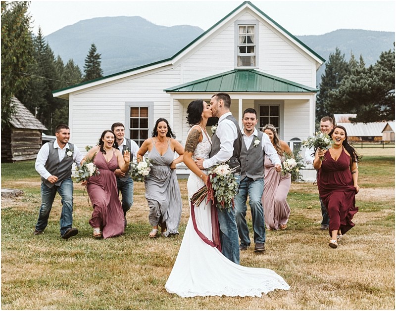 Premier snohomish & seattle wedding photographer | gsquared weddings photography a bride and groom kiss in front of a white house surrounded by their joyful wedding party running toward them all smiling and holding bouquets with a stunning snohomish mountain backdropa perfect seattle wedding moment | serving snohomish seattle                   & beyond