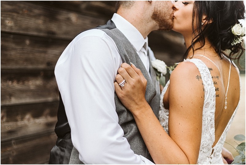 Premier snohomish & seattle wedding photographer | gsquared weddings photography a bride and groom share a kiss beside a wooden wall at their snohomish wedding The bride in a white lace dress with her hair up and a flower in it shows off her wedding ring while holding the grooms shoulder | serving snohomish seattle                   & beyond