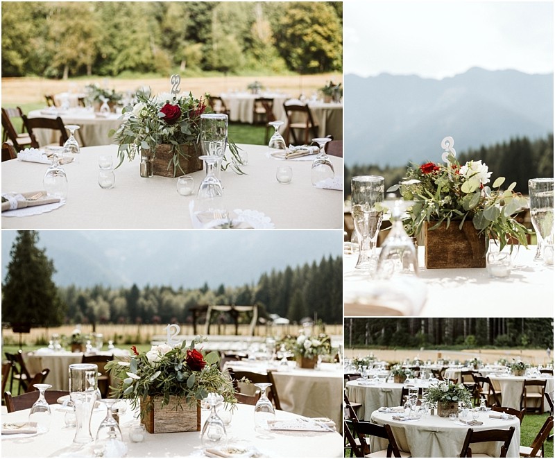 Premier snohomish & seattle wedding photographer | gsquared weddings photography tables set outdoors with cream tablecloths wooden chairs and rustic centerpieces of greenery and red flowers in wooden boxes Mountains trees and an open field create a scenic snohomish wedding backdrop under a bright sky | serving snohomish seattle                   & beyond