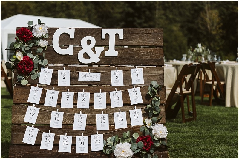 Premier snohomish & seattle wedding photographer | gsquared weddings photography a rustic wooden wedding seating chart perfect for a snohomish or seattle wedding is adorned with flowers and large white letters c & t Individual cards display table assignments outdoors with reception tables and chairs in the background | serving snohomish seattle                   & beyond