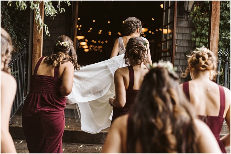 Premier snohomish & seattle wedding photographer | gsquared weddings photography five women in burgundy dresses likely bridesmaids walk up steps into a snohomish wedding venue One woman lifts the train of a brides white dress as they enter warmly lit by string lights inside Perfect for a seattle engagement celebration | serving snohomish seattle                   & beyond