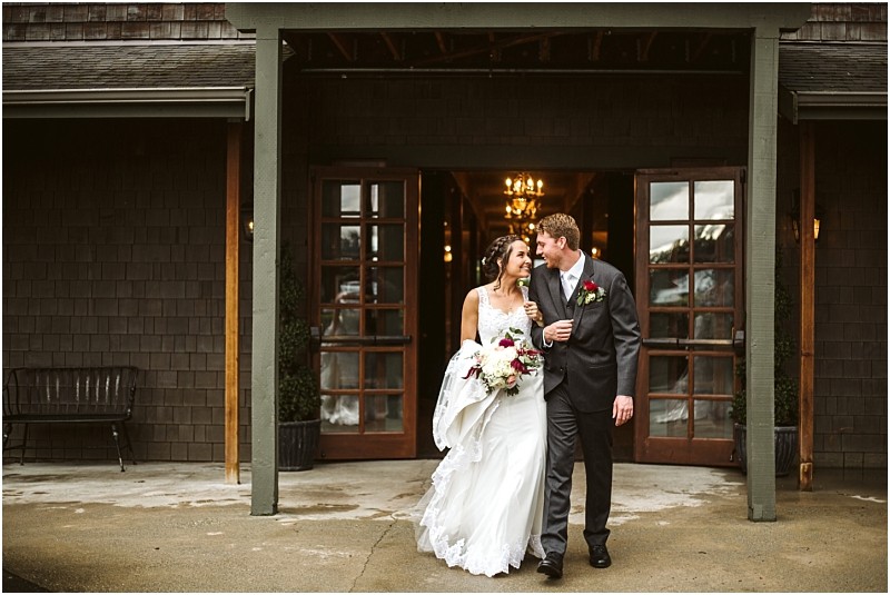 Premier snohomish & seattle wedding photographer | gsquared weddings photography a bride and groom smiling and holding hands walk out of a rustic building with wooden doors after their snohomish wedding The bride in a white gown holds a bouquet the groom wears a dark suit and boutonniere | serving snohomish seattle                   & beyond