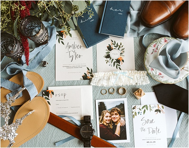Premier snohomish & seattle wedding photographer | gsquared weddings photography flat lay of snohomish wedding items on a light blue surface featuring invitations rings a save the date card garter wristwatch brown shoes sandals blue vow books a couples photo and floral accentsperfect seattle engagement inspiration | serving snohomish seattle                   & beyond